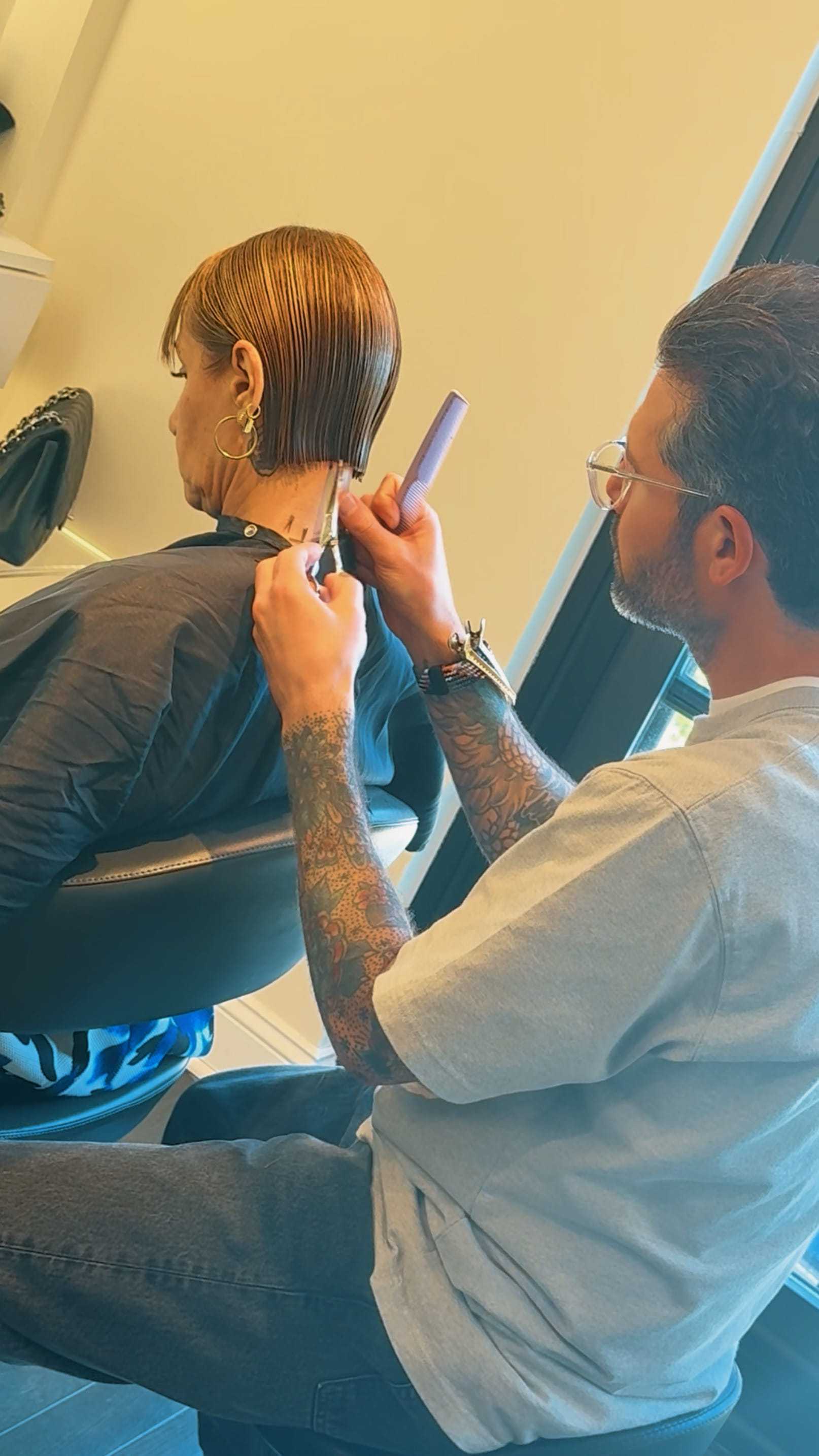 Hair stylist precisely cutting a woman's short, wet hair at a salon.