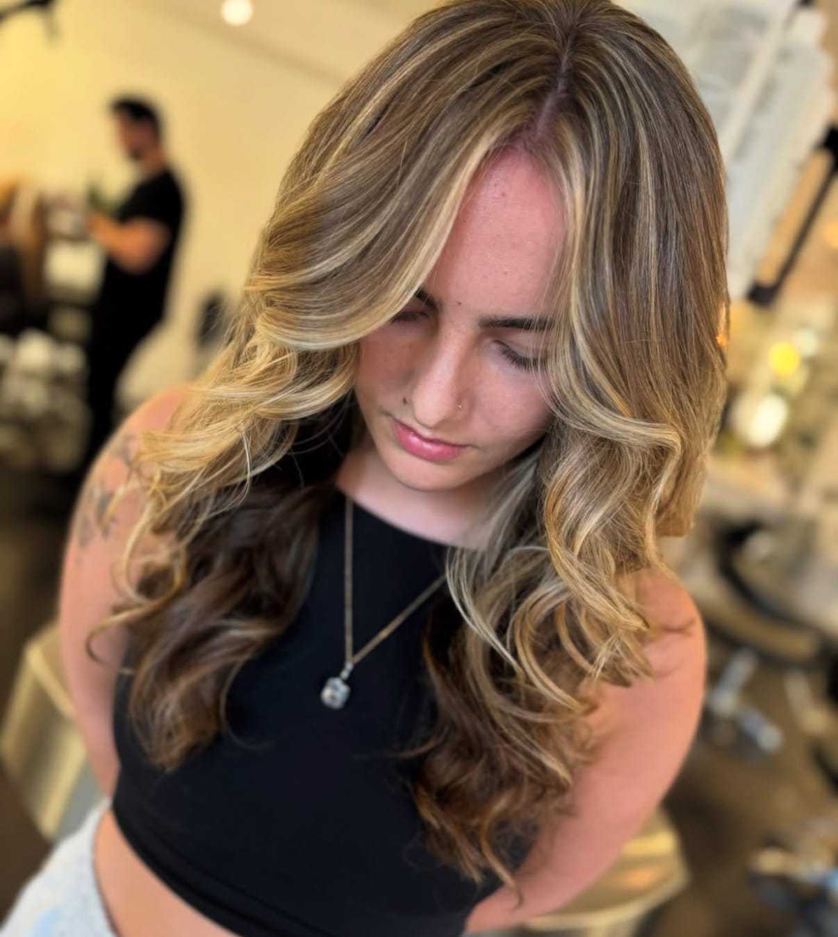 Woman with long, wavy blonde hair looking down in a salon setting.