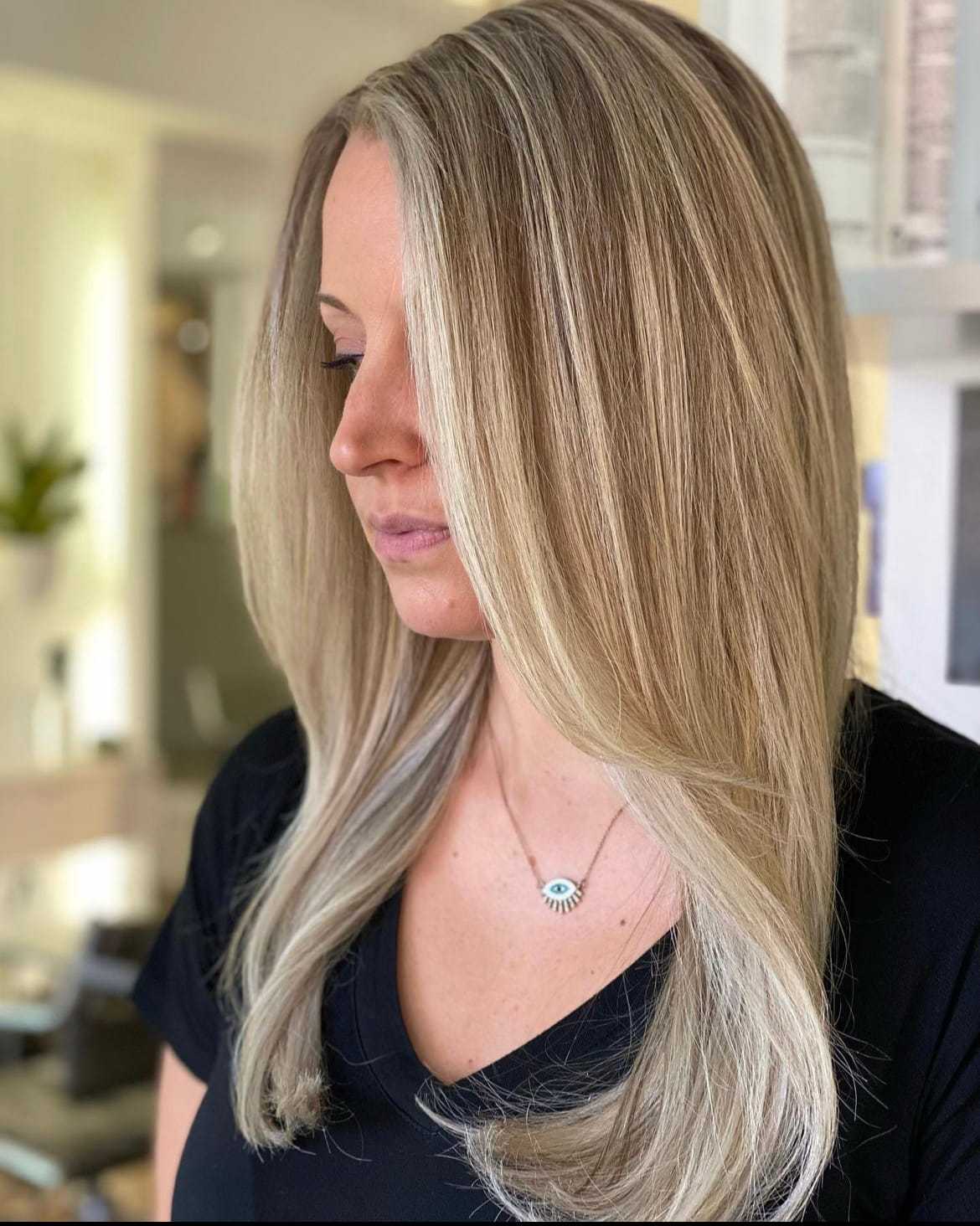 Woman with long, straight blonde hair, wearing a black top and a necklace with an eye pendant.